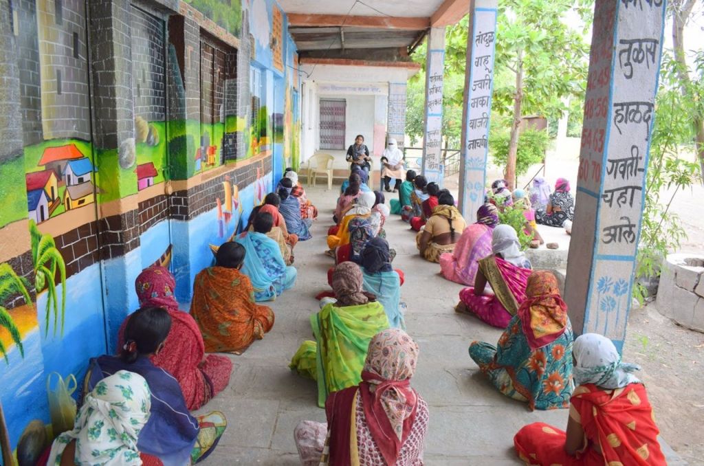 Savine Ventures workshop for rural women, showing participants seated in rows on a long stone veranda alongside educational murals during a CSR outreach program